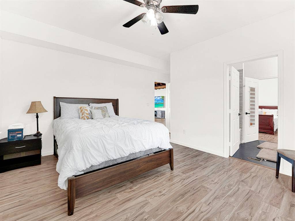 Room featuring wood-finish flooring, a multi-blade ceiling fan with integrated lighting, and high-contrast interior doors