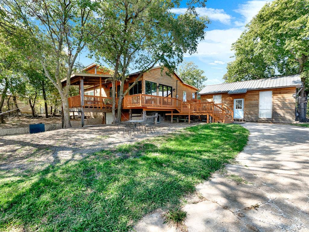 Exterior featuring wood siding, expansive wraparound elevated wood deck, metal roofing, concrete driveway, and mature tree canopy