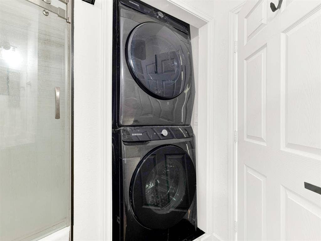 Stackable, front-load washer and dryer in a black finish, accompanied by a glass-panel shower door with a metallic pull handle and a white paneled door