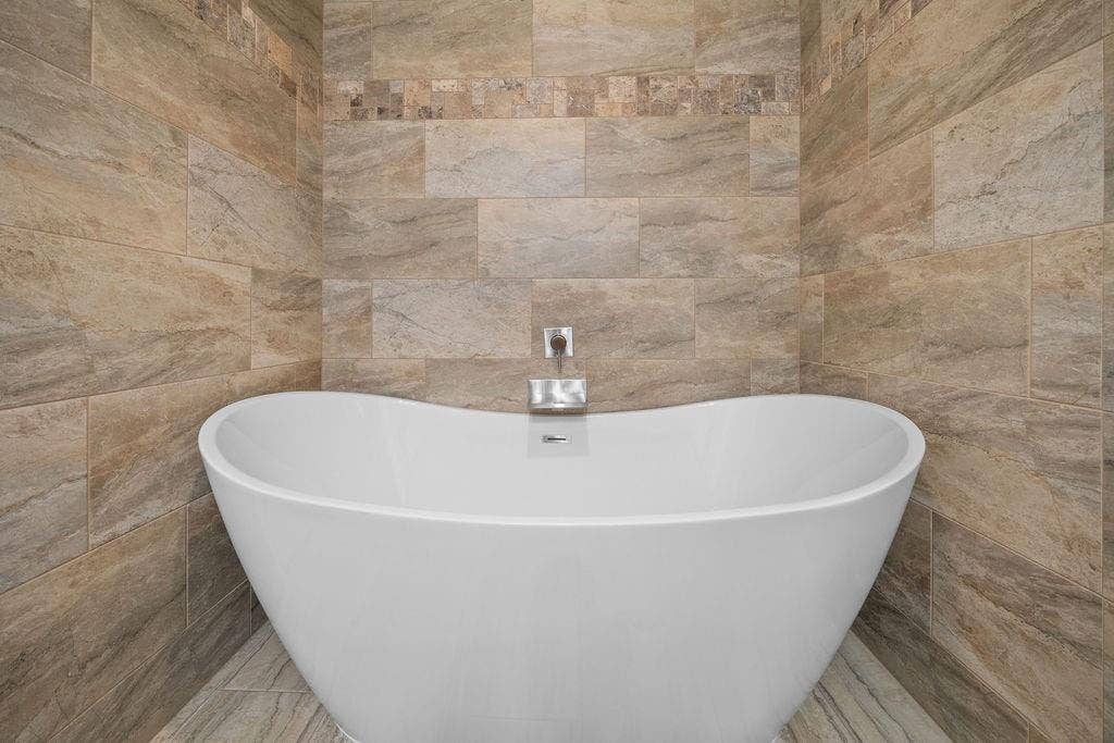 15993 Big Oak Bay Road, Tyler, TX 75707 Freestanding white soaking tub featuring a wall-mounted faucet and surround of large-format stone-finish tile with integrated mosaic accent banding