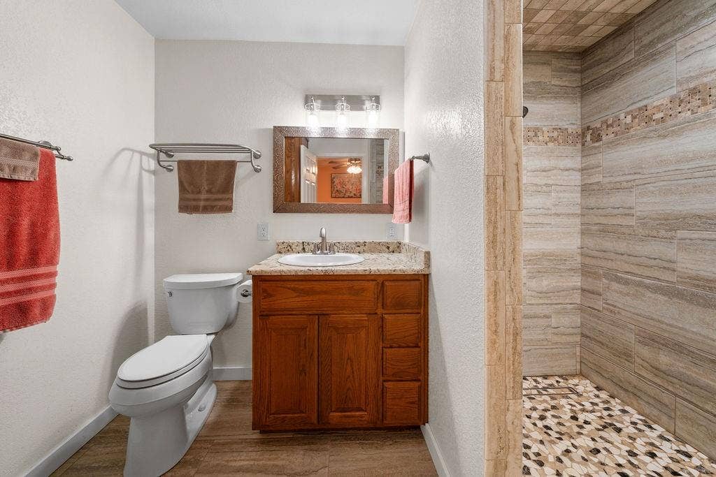 15993 Big Oak Bay Road, Tyler, TX 75707 Bathroom featuring a wood-finish vanity with a stone countertop, an integrated sink, an expansive walk-in shower with decorative tile accents, and wood-finish flooring