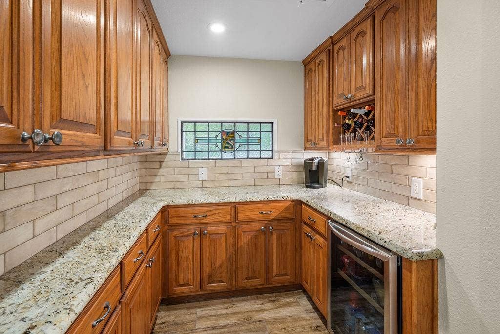 15993 Big Oak Bay Road, Tyler, TX 75707 Custom cabinetry with integrated wine storage, stone countertops, subway tile backsplash, stained glass accent window, and built-in under-counter beverage refrigerator