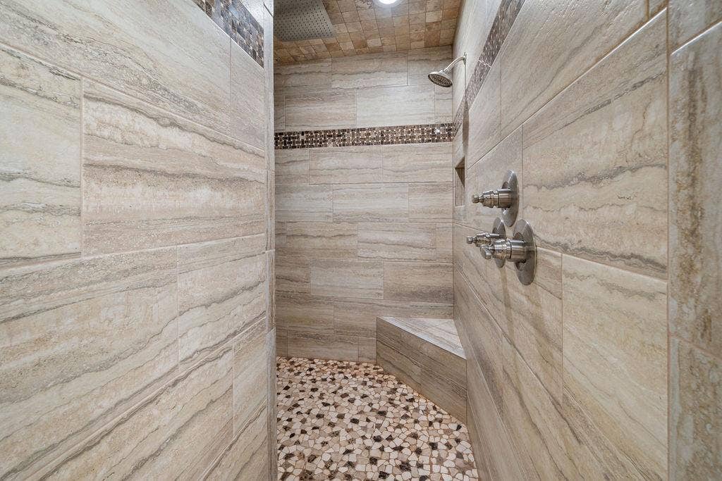 15993 Big Oak Bay Road, Tyler, TX 75707 Walk-in shower featuring large-format neutral-toned wall tile, decorative mosaic tile accents, a built-in corner bench, a ceiling-mounted rainfall showerhead, and a multi-handle faucet system