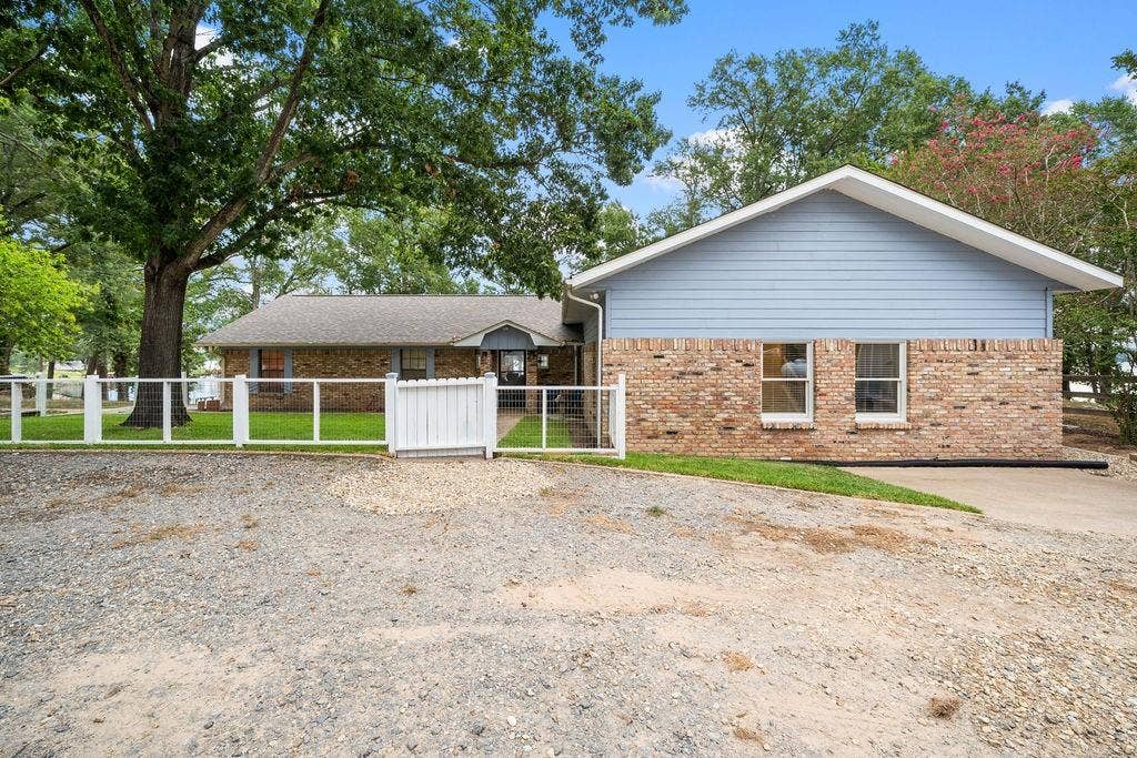 15993 Big Oak Bay Road, Tyler, TX 75707 Single-story exterior featuring a combination of brick and lap siding, a pitched roofline, and a fenced front yard with mature trees