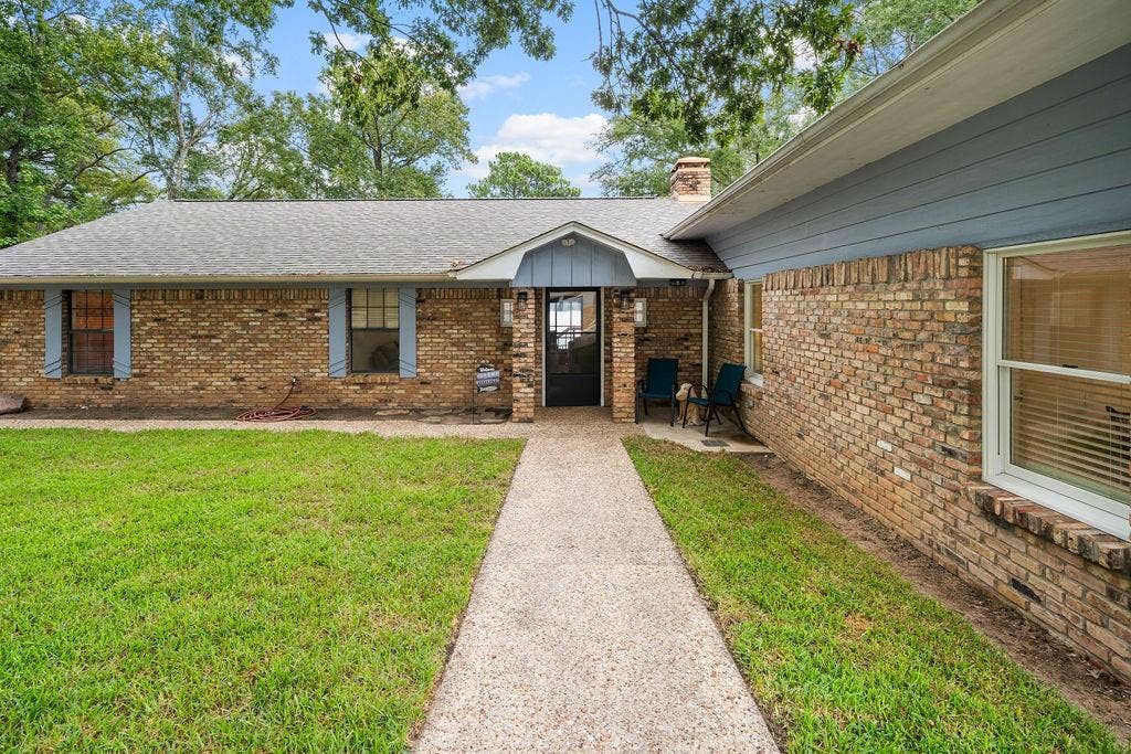 15993 Big Oak Bay Road, Tyler, TX 75707 Single-story brick exterior featuring blue-toned siding, a covered entryway with a gabled roofline, a masonry chimney, and a concrete walkway