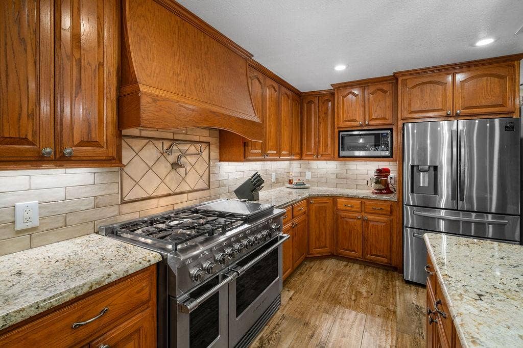 15993 Big Oak Bay Road, Tyler, TX 75707 Kitchen featuring raised-panel wood cabinetry, natural stone countertops, a multi-burner stainless steel gas range with a custom wood-enclosed vent hood, and wood-finish flooring