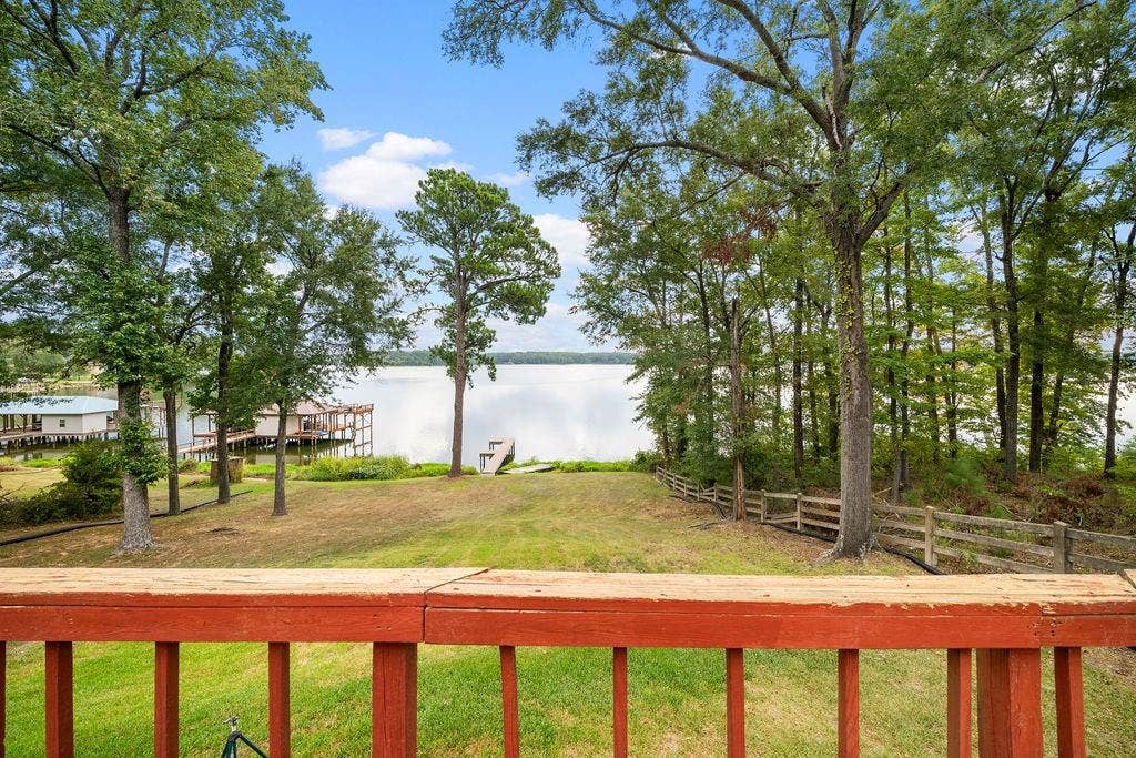 15993 Big Oak Bay Road, Tyler, TX 75707 Elevated wood-railing deck overlooking a grassy backyard with mature trees, a wooden rail fence, and direct waterfront access including a private dock