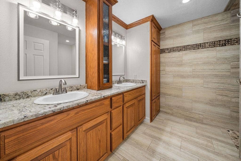 15993 Big Oak Bay Road, Tyler, TX 75707 Double vanity featuring wood cabinetry, stone-patterned countertops, integrated storage tower, and dual undermount sinks with polished hardware
