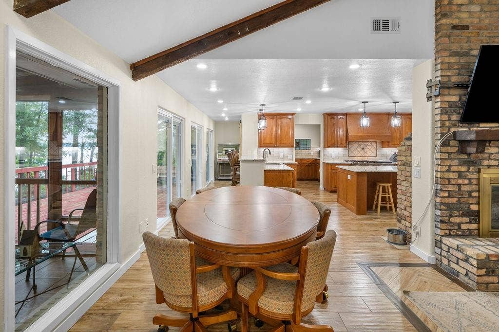 15993 Big Oak Bay Road, Tyler, TX 75707 Vaulted ceilings with exposed wooden beams, brick-surround fireplace, wood-finish tile flooring, recessed lighting, and multiple sliding glass doors