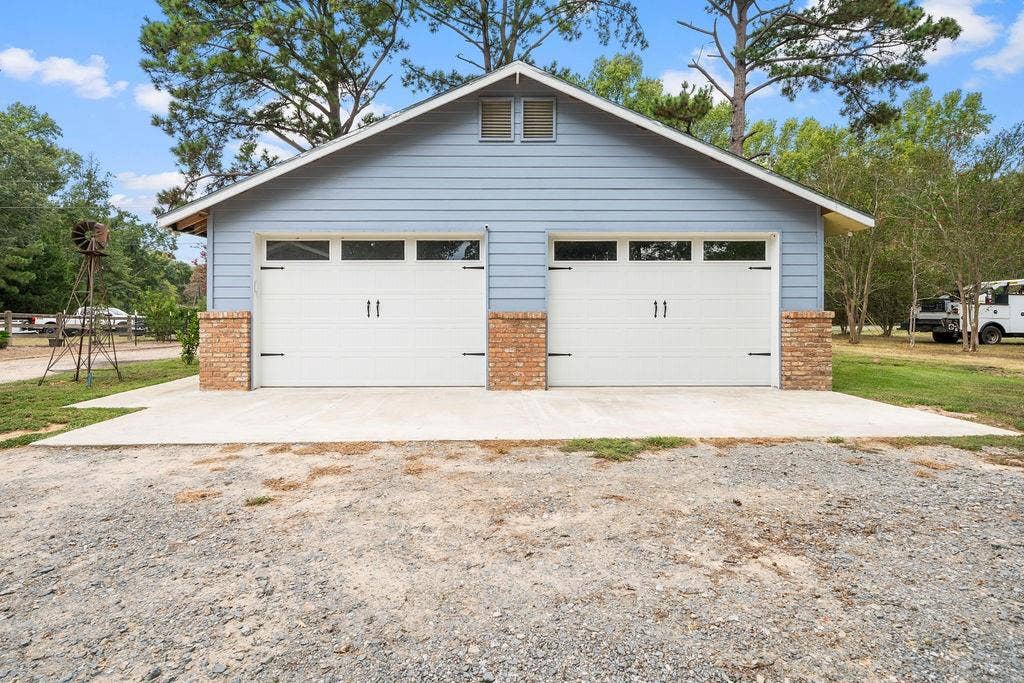 15993 Big Oak Bay Road, Tyler, TX 75707 Detached two-car garage featuring blue horizontal siding, dual overhead doors with windows, brick pillar accents, and a concrete apron