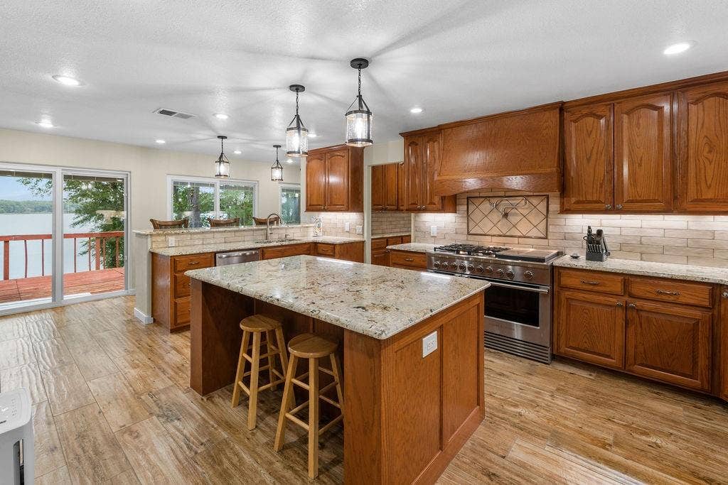 15993 Big Oak Bay Road, Tyler, TX 75707 Kitchen featuring wood cabinetry, stone countertops, a center island, stainless steel range with a custom hood, and wood-finish flooring