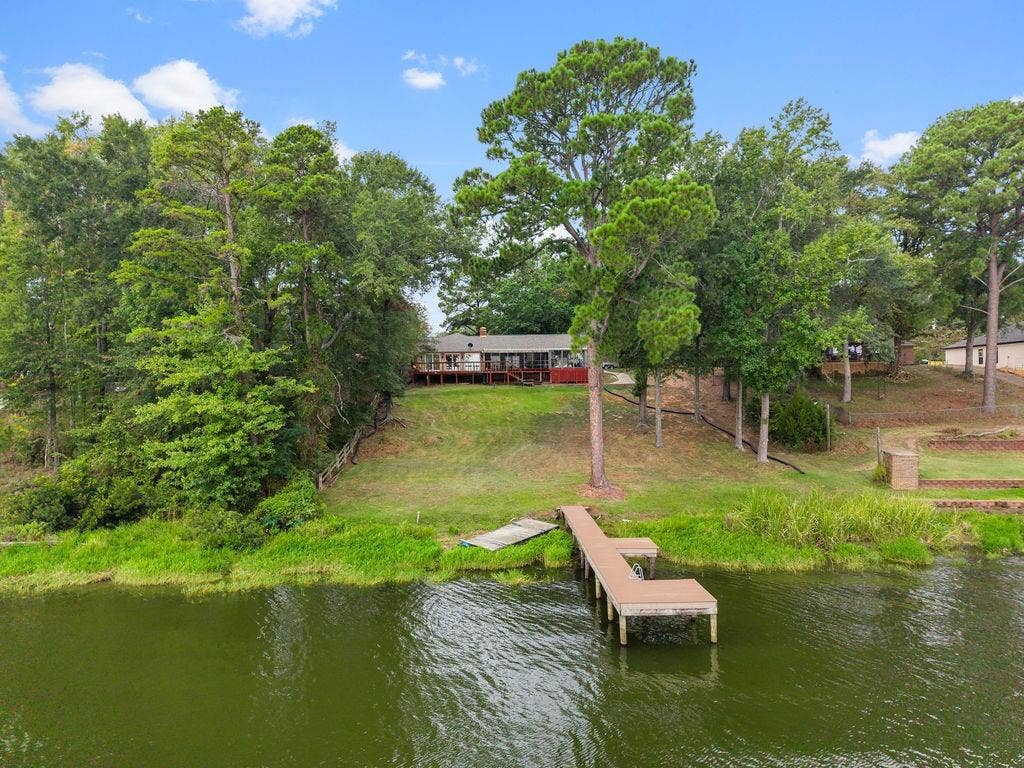 15993 Big Oak Bay Road, Tyler, TX 75707 Waterfront property featuring a private wooden pier, expansive sloped lawn, mature trees, and a raised exterior deck