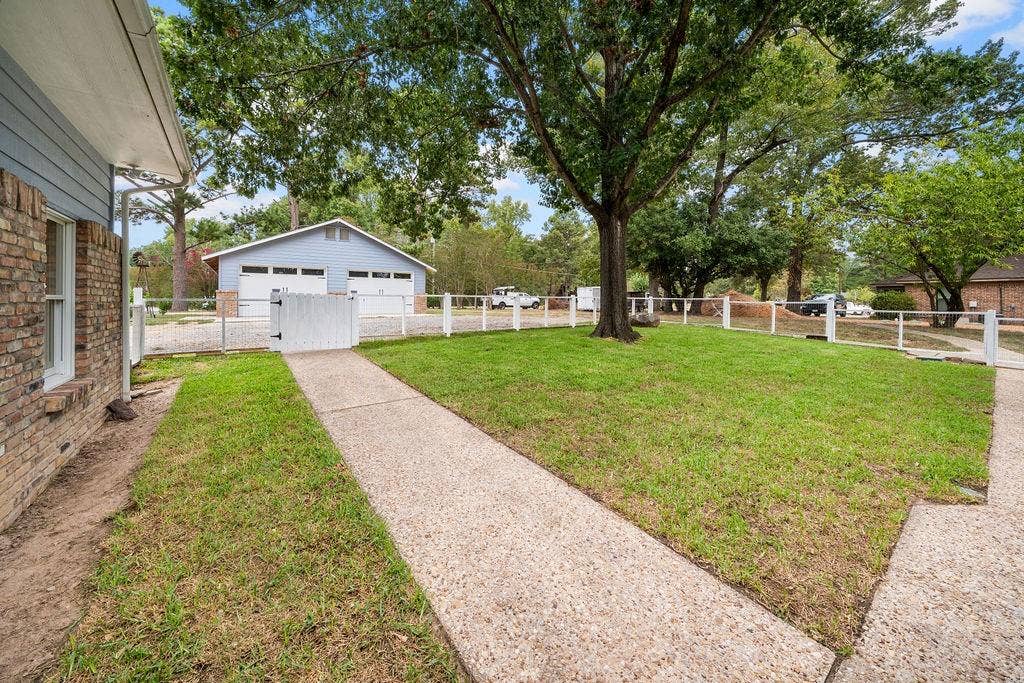 15993 Big Oak Bay Road, Tyler, TX 75707 Fenced backyard featuring a concrete walkway, mature trees, a detached two-car garage, and brick and siding exterior cladding