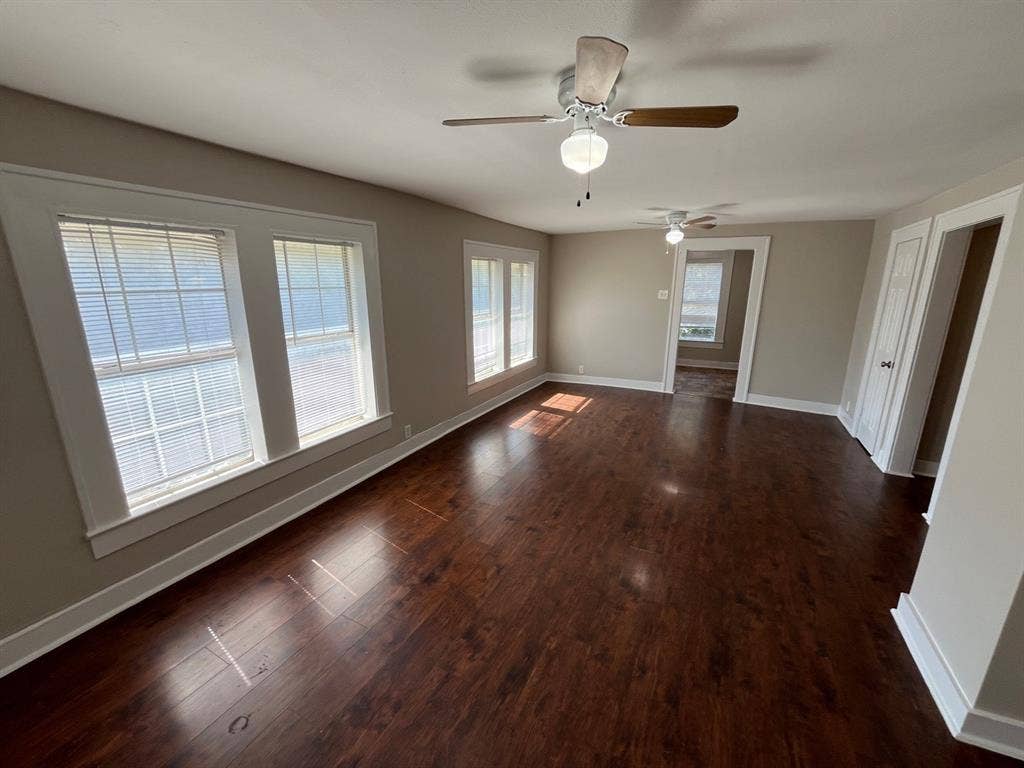 Interior space featuring dark wood-finish flooring, multi-pane windows with trim, and two ceiling fans