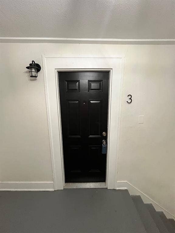 Six-panel black entry door featuring a matte metal door handle, brass-tone peephole, and matching black wall-mounted lantern-style light fixture with white casing trim