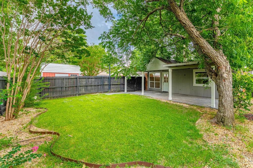 3618 Flagstone Avenue, Rowlett, TX 75088 Backyard featuring a covered patio, mature shade trees, perimeter wood fencing, and a manicured lawn