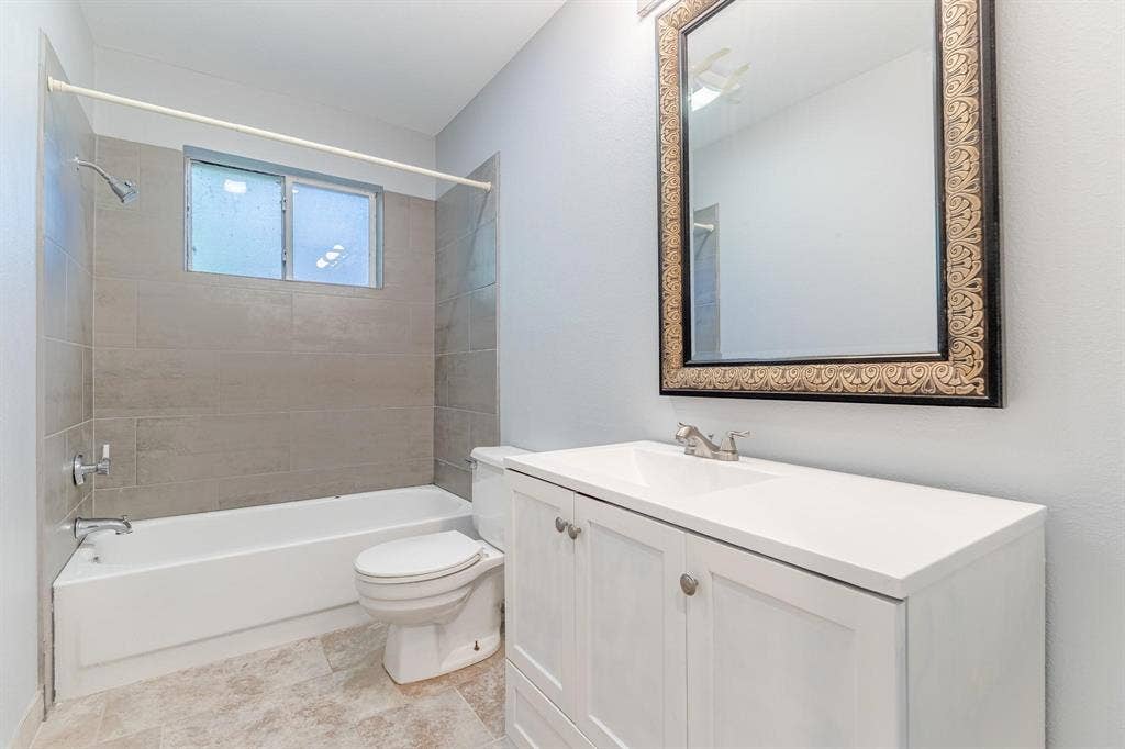 3618 Flagstone Avenue, Rowlett, TX 75088 Bathroom featuring a white vanity cabinet with a solid surface countertop, rectangular under-mount sink, tile tub surround, and tile flooring