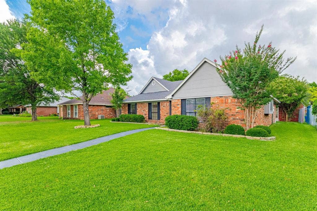3618 Flagstone Avenue, Rowlett, TX 75088 Single-story residence featuring a brick and horizontal siding exterior, dual-gable roofline, concrete walkway, and manicured landscaping with mature trees