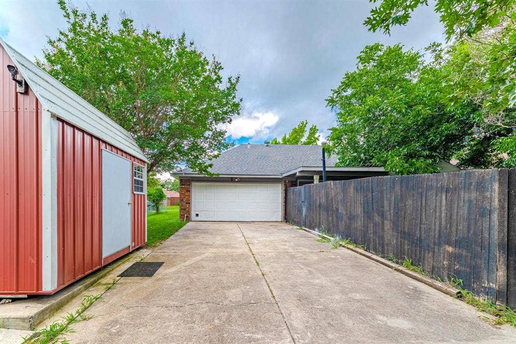 3618 Flagstone Avenue, Rowlett, TX 75088 Concrete driveway with an attached garage, featuring a metal storage structure and privacy fencing