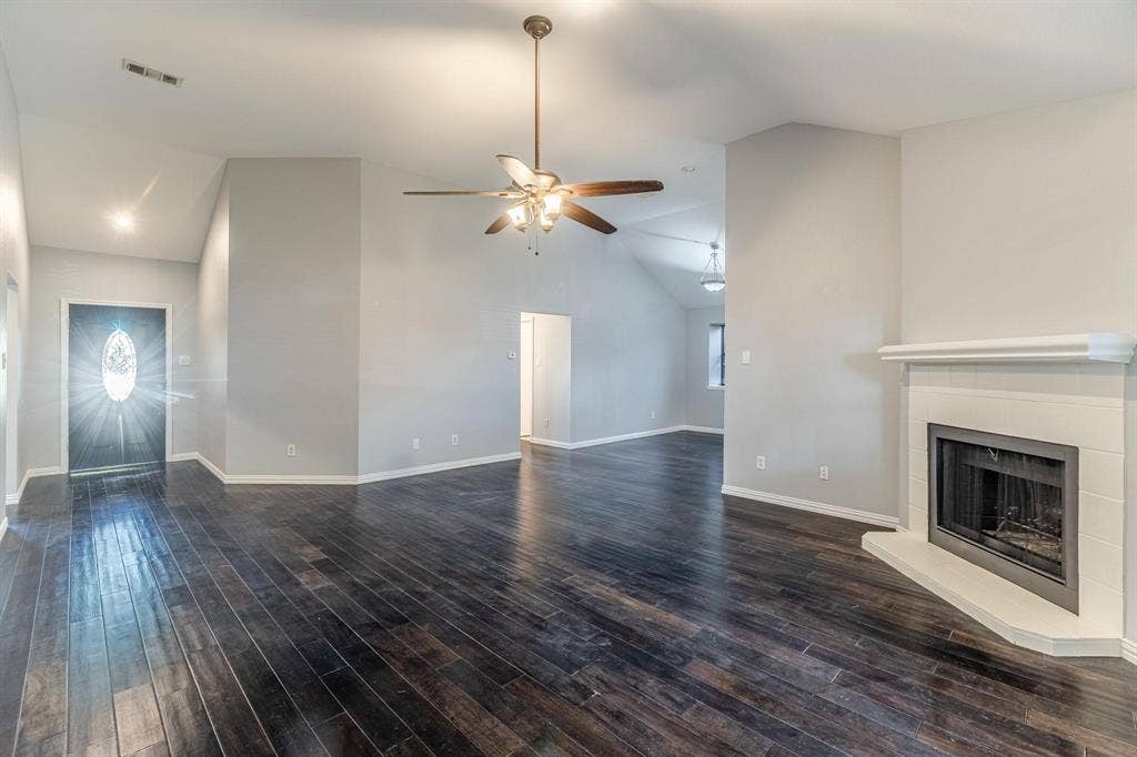 3618 Flagstone Avenue, Rowlett, TX 75088 Vaulted ceilings featuring a central ceiling fan, dark wood-finish flooring, and a fireplace with a white tile surround and mantel