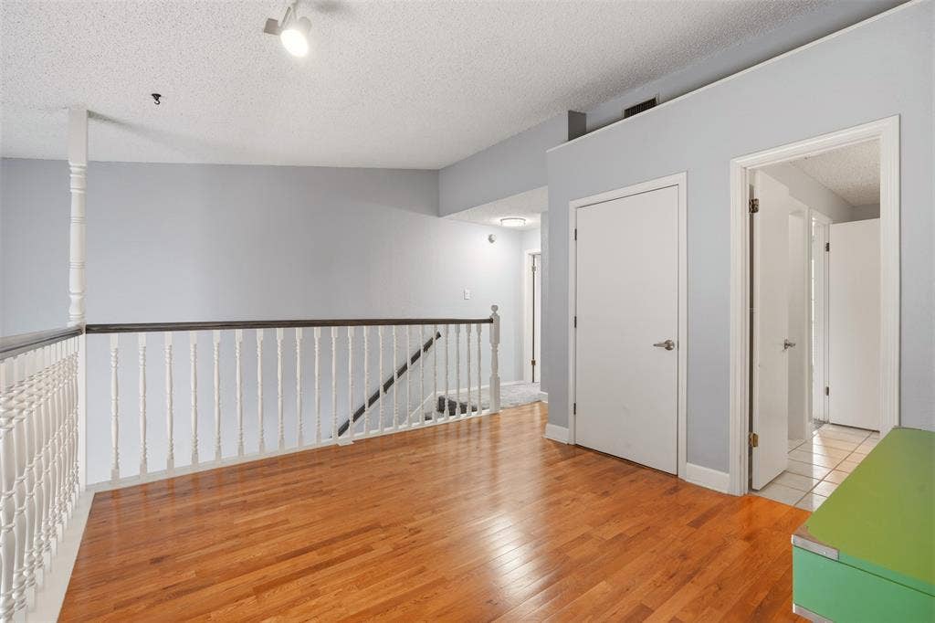 14333 Preston Road, #806, Dallas, TX 75254 Wood-finish flooring, white spindle staircase railing with a dark wood-finish handrail, and interior doors with brushed nickel hardware