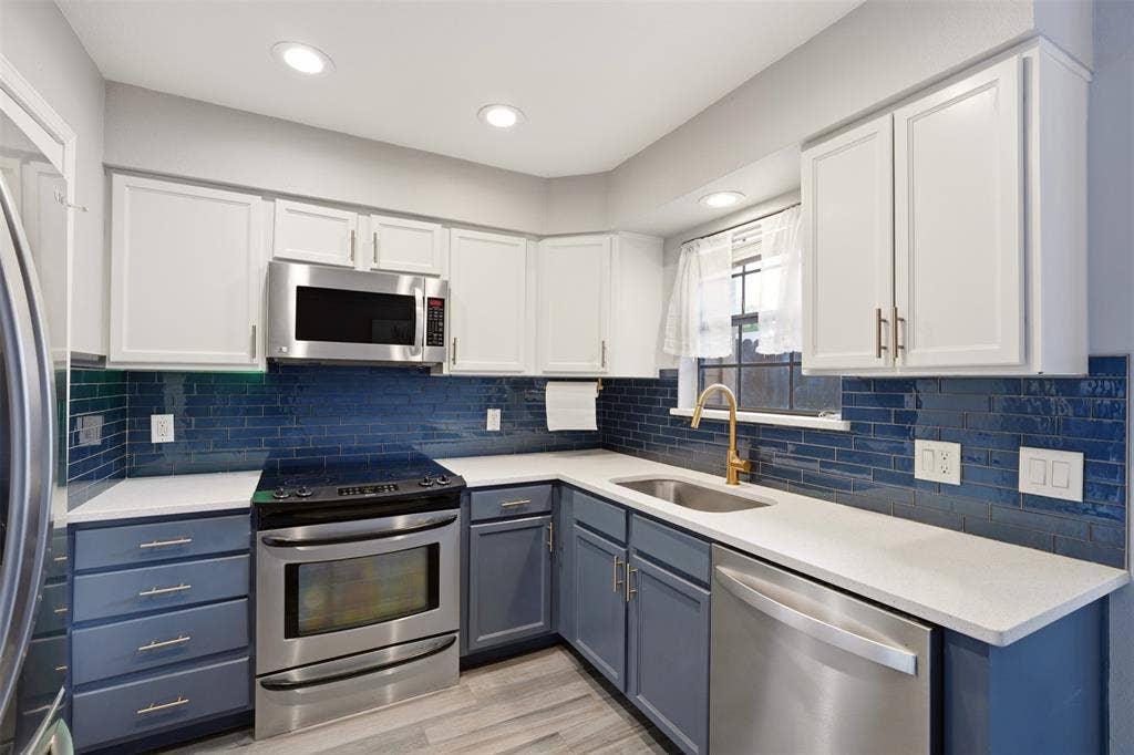 14333 Preston Road, #806, Dallas, TX 75254 Kitchen featuring two-tone shaker-style cabinetry, deep blue subway tile backsplash, quartz countertops, stainless steel appliances, and a brass-finish faucet