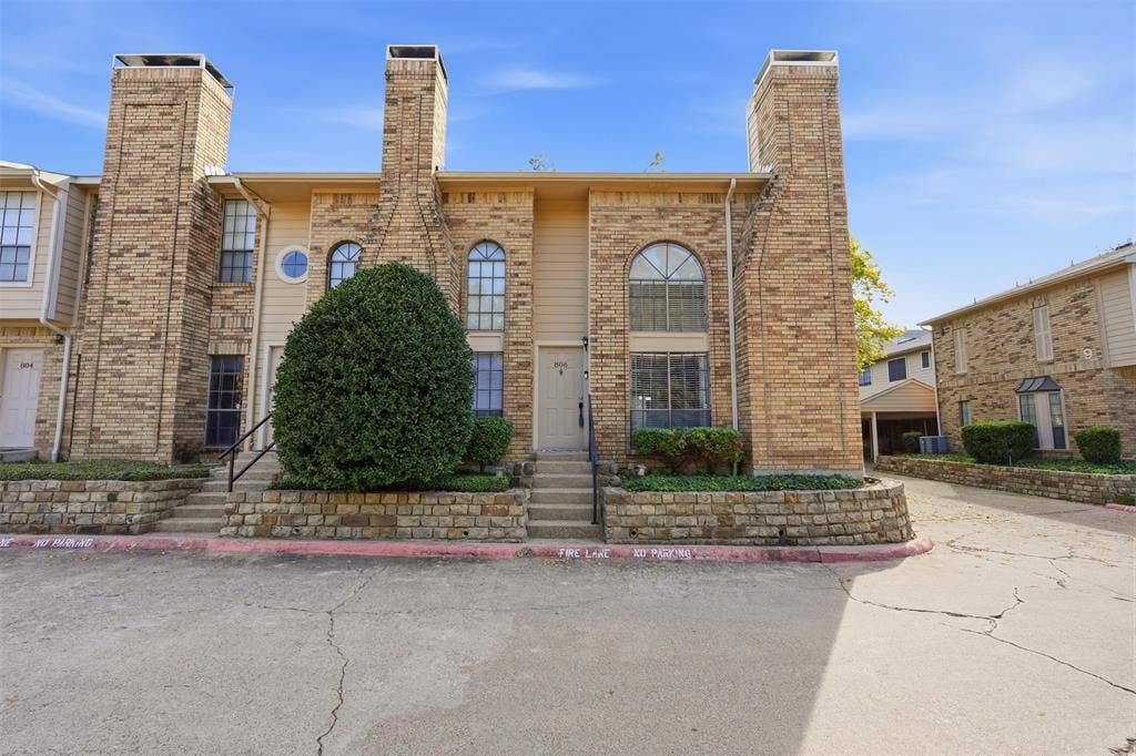 14333 Preston Road, #806, Dallas, TX 75254 Multi-level brick exterior featuring dual masonry chimneys, arched windows, and a stacked stone retaining wall