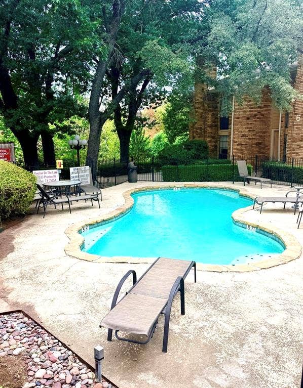 14333 Preston Road, #806, Dallas, TX 75254 Swimming pool featuring a natural stone coping, concrete decking, metal perimeter fencing, and mature trees