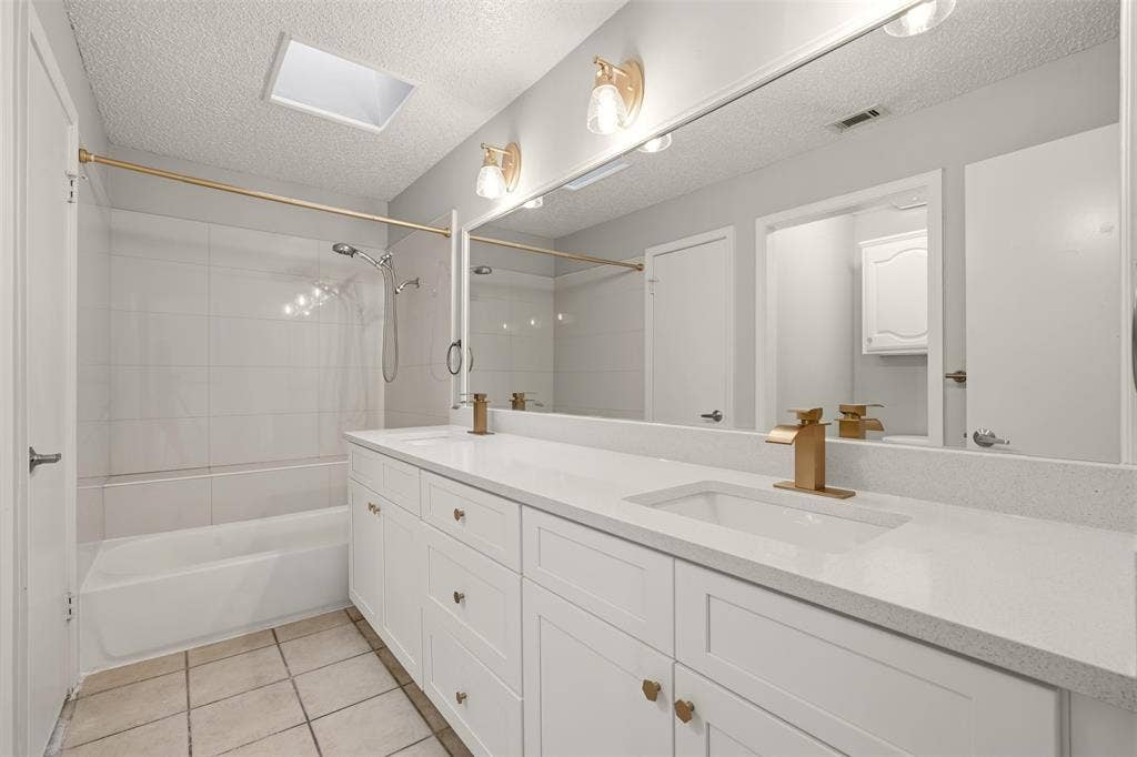 14333 Preston Road, #806, Dallas, TX 75254 Full-width vanity with white cabinetry and quartz countertop, dual integrated sinks, brass-finish hardware, and built-in skylight