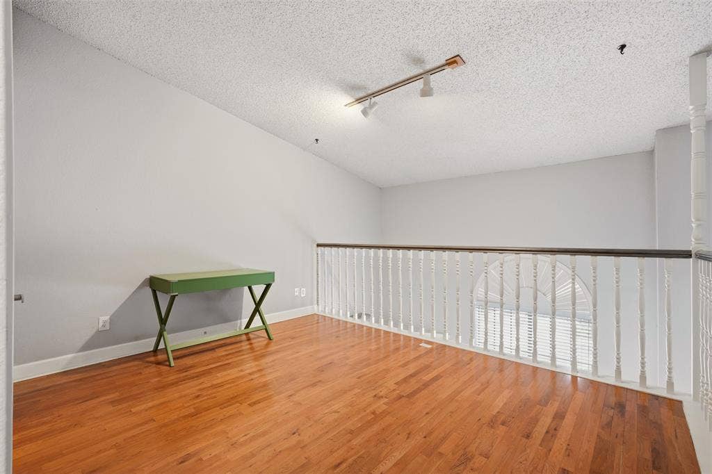14333 Preston Road, #806, Dallas, TX 75254 Open-plan space featuring wood-finish flooring, vaulted ceiling, white painted railing with a dark wood-finish cap, and ceiling-mounted track lighting