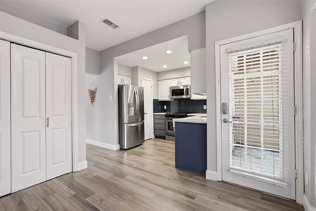 14333 Preston Road, #806, Dallas, TX 75254 Kitchen featuring stainless steel appliances, dark-toned subway tile backsplash, white shaker-style cabinetry, a contrasting blue base cabinet, and wood-finish flooring