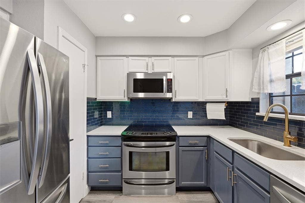 14333 Preston Road, #806, Dallas, TX 75254 Kitchen featuring white upper cabinetry, blue lower cabinetry, stainless steel appliances, quartz countertops, and blue subway tile backsplash