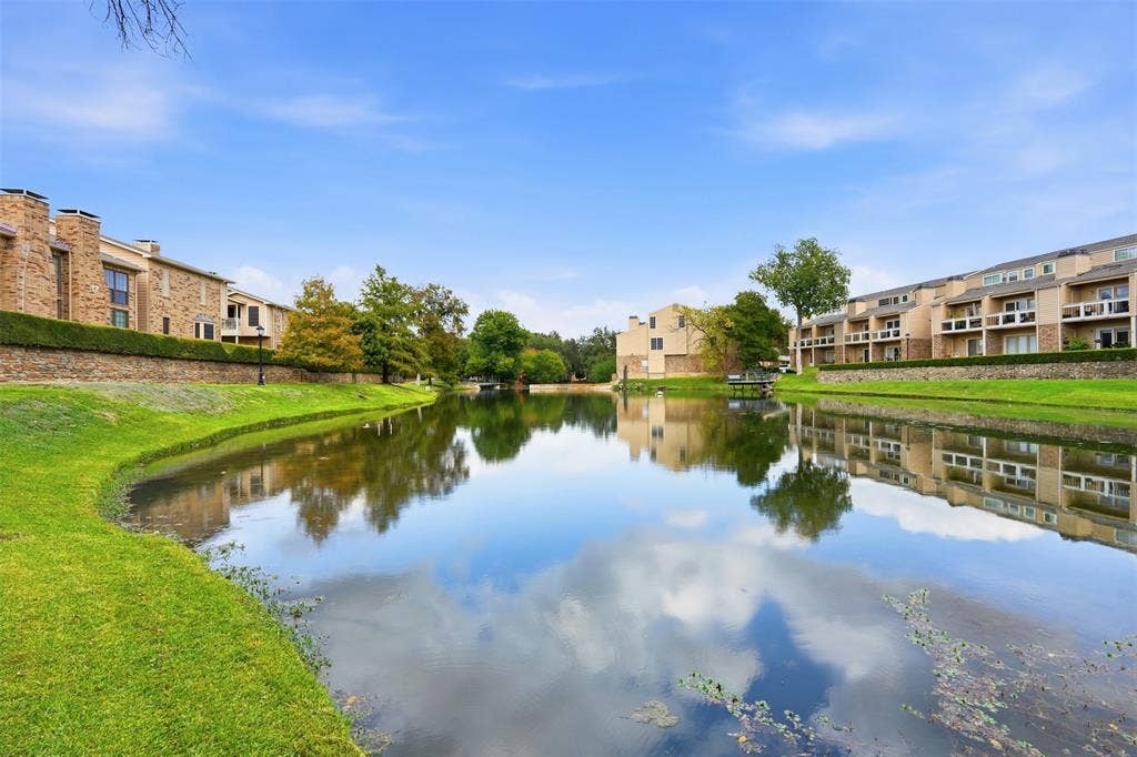 14333 Preston Road, #806, Dallas, TX 75254 Waterfront property featuring a central pond, expansive manicured lawn, stone retaining walls, mature trees, and multi-story building exteriors with attached balconies