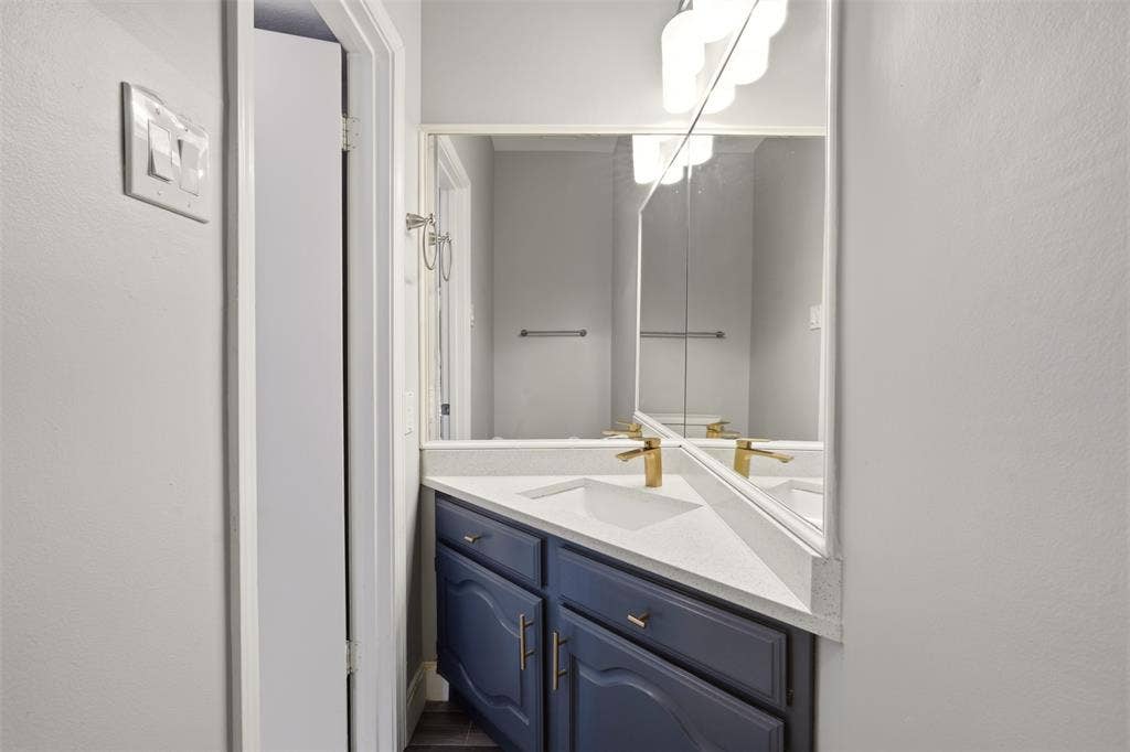 14333 Preston Road, #806, Dallas, TX 75254 Corner vanity featuring navy cabinetry, stone-composite countertop, integrated sink, gold-tone faucet, and expansive wall mirror