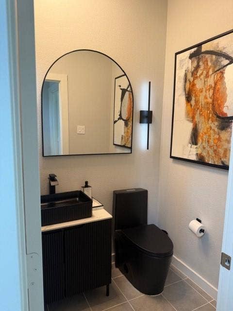 2416 Adenmore Lane, Forney, TX 75126 Modern vanity with a rectangular sink, matte black faucet, arched wall mirror, vertical sconce lighting, and a black toilet