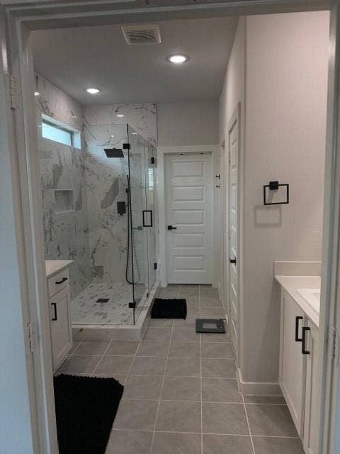 2416 Adenmore Lane, Forney, TX 75126 Walk-in shower featuring floor-to-ceiling stone-pattern tile, a glass enclosure, and a wall-mounted shower head, complemented by white cabinetry with matte black hardware and light-toned tile flooring