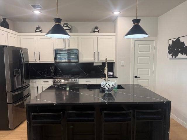 2416 Adenmore Lane, Forney, TX 75126 Kitchen featuring white cabinetry, black stone-patterned countertops, a matching central island with built-in sink, stainless steel appliances, and dual pendant lighting