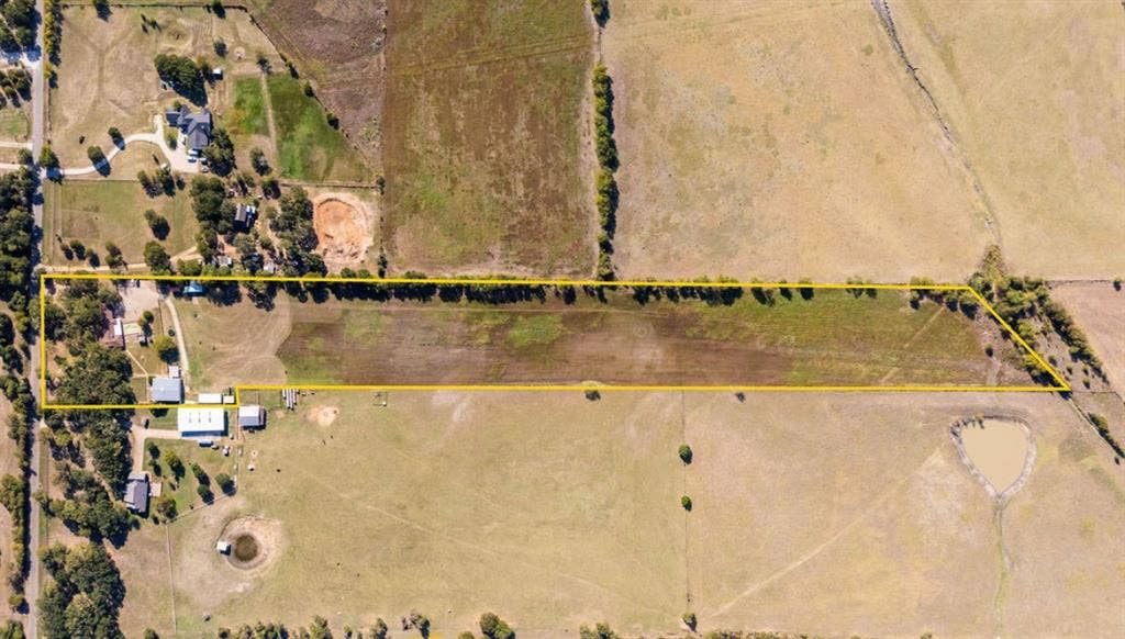 Aerial view of expansive acreage featuring mature tree lines, fenced perimeter, multiple outbuildings, and open pasture land