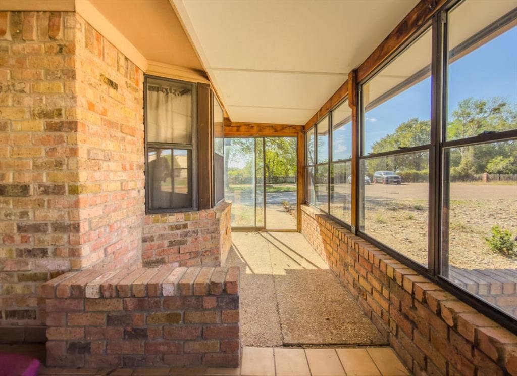 Enclosed sunroom featuring exposed brick walls, a built-in brick bench, expansive windows with dark frames, and sliding glass door access