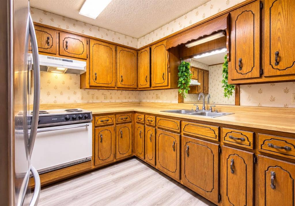 Kitchen featuring wood cabinetry with arched panel detailing, laminate countertops, a stainless steel double-basin sink with a gooseneck faucet, a white freestanding range, and wood-finish flooring