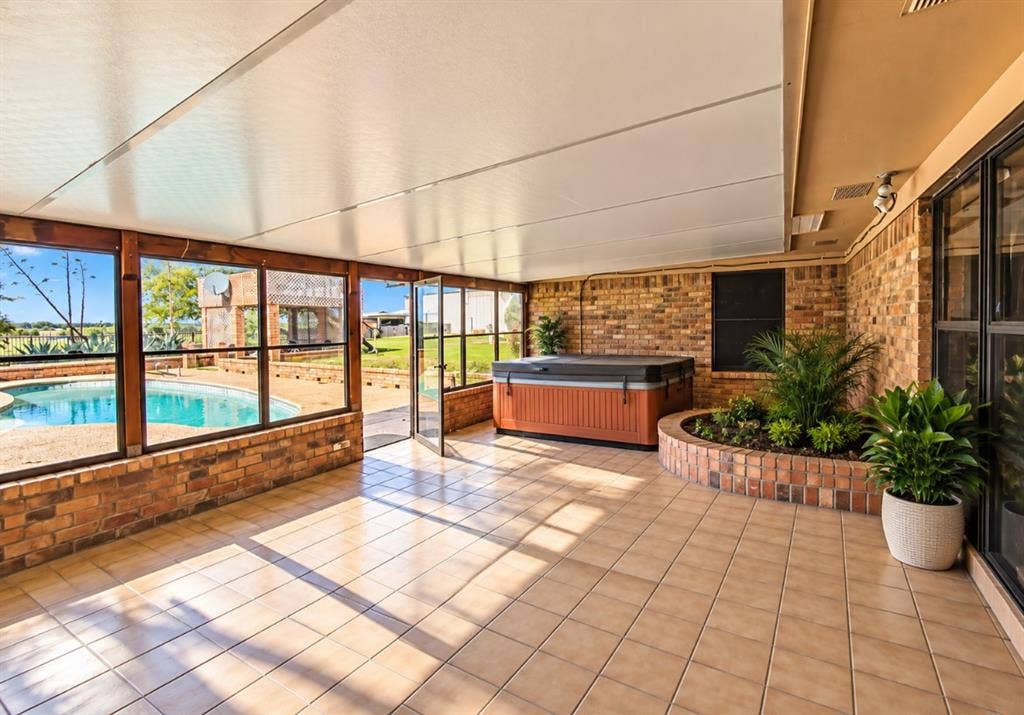 Enclosed patio featuring a tiled floor, brick wall construction, built-in circular brick planter, and metal-framed screen windows