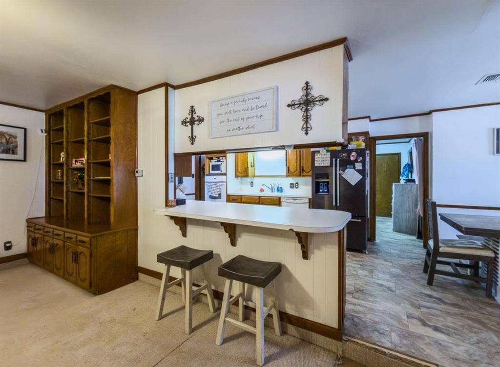 Built-in floor-to-ceiling wooden shelving unit, pass-through kitchen window with a breakfast bar, and tile flooring