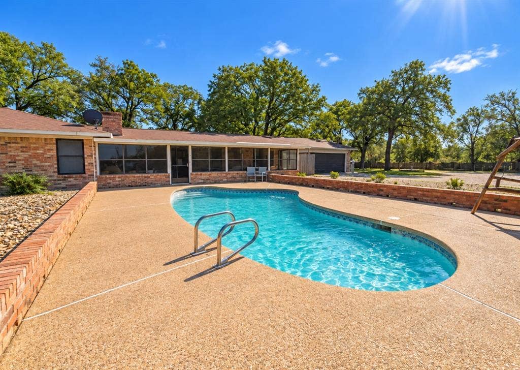 In-ground pool with aggregate decking and a decorative brick retaining wall