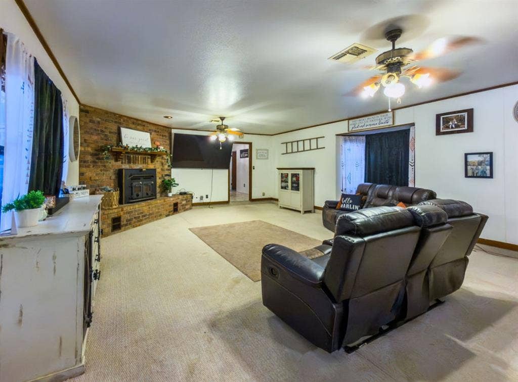 Brick fireplace with a wood mantel, dual ceiling fans, and a bay window