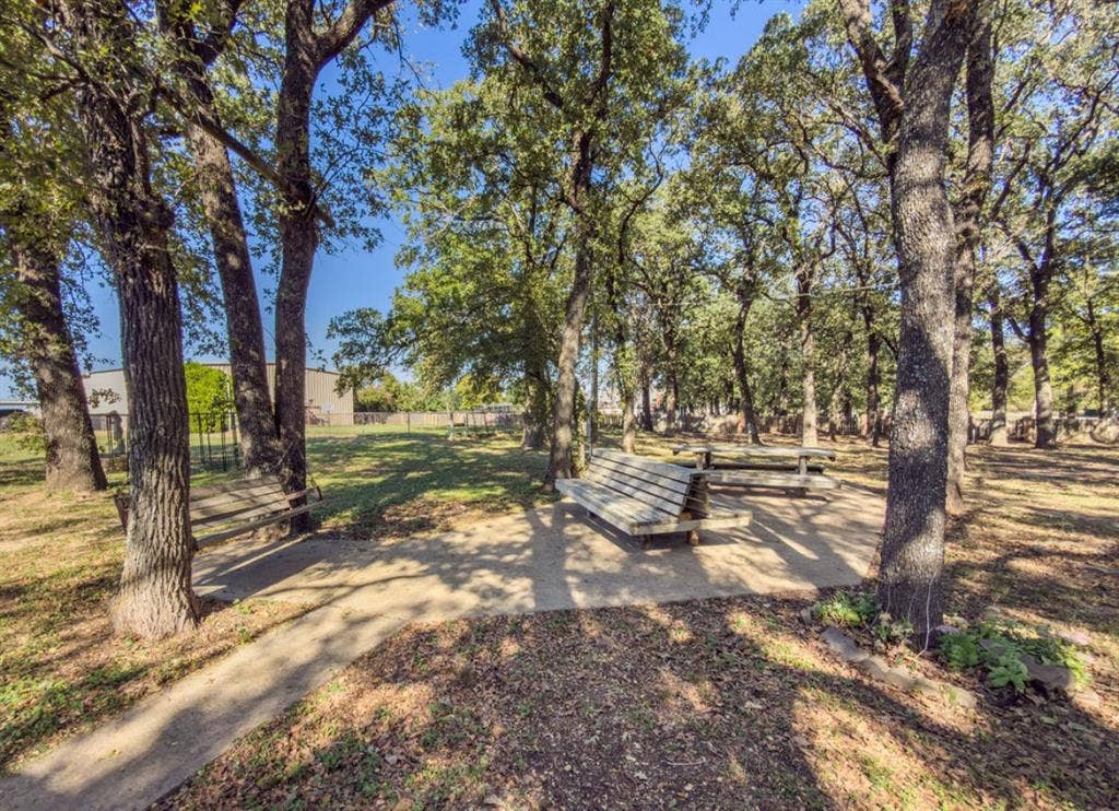 Outdoor space featuring a concrete pathway, built-in wooden bench seating, a wooden picnic table, and mature trees