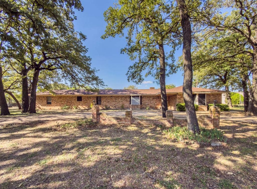 Single-story brick exterior featuring a sprawling layout, low-pitch roofline, and an integrated brick retaining wall, all set among mature trees