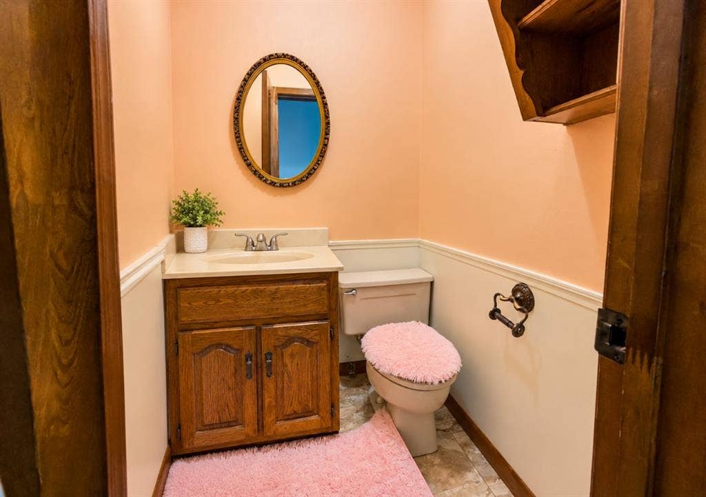 Wood cabinetry vanity featuring a solid surface countertop, an oval wall-mounted mirror with an ornate frame, built-in wooden shelving, and decorative chair rail trim