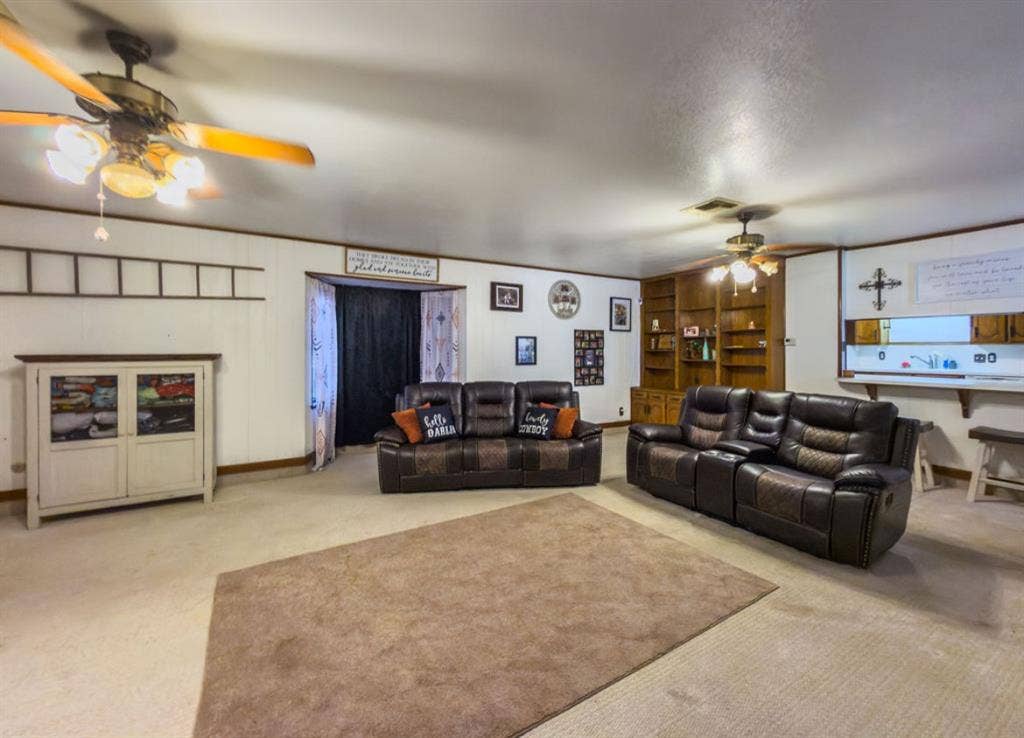 Spacious room featuring wood-finish built-in shelving, two ceiling fans with integrated light fixtures, and a pass-through opening to additional living space