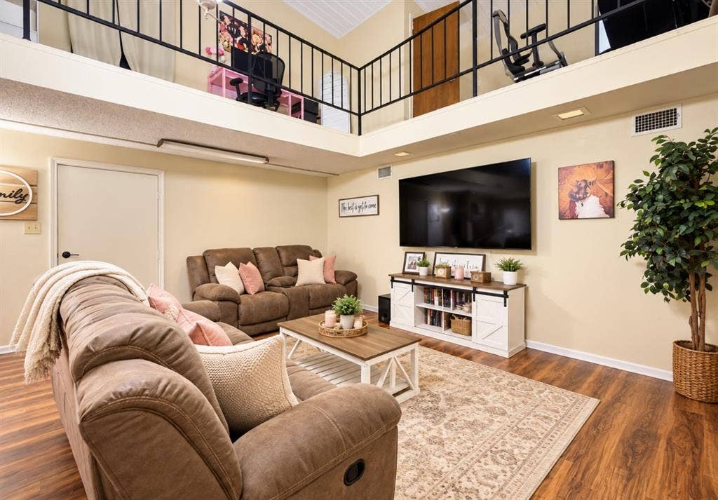 Vaulted ceilings, open loft level with black metal railings, and wood-finish flooring