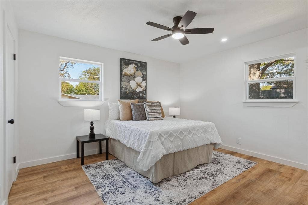 828 Melrose Drive, Richardson, TX 75234 Bedroom featuring wood-finish flooring, dual windows with sills, and a centrally mounted ceiling fan with integrated lighting